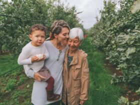 A woman is seen in an orchard, holding her son. She has her arm around her mother.