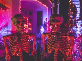 two skeletons talking to each other one with jaw dropped in shock. Halloween lights in background.