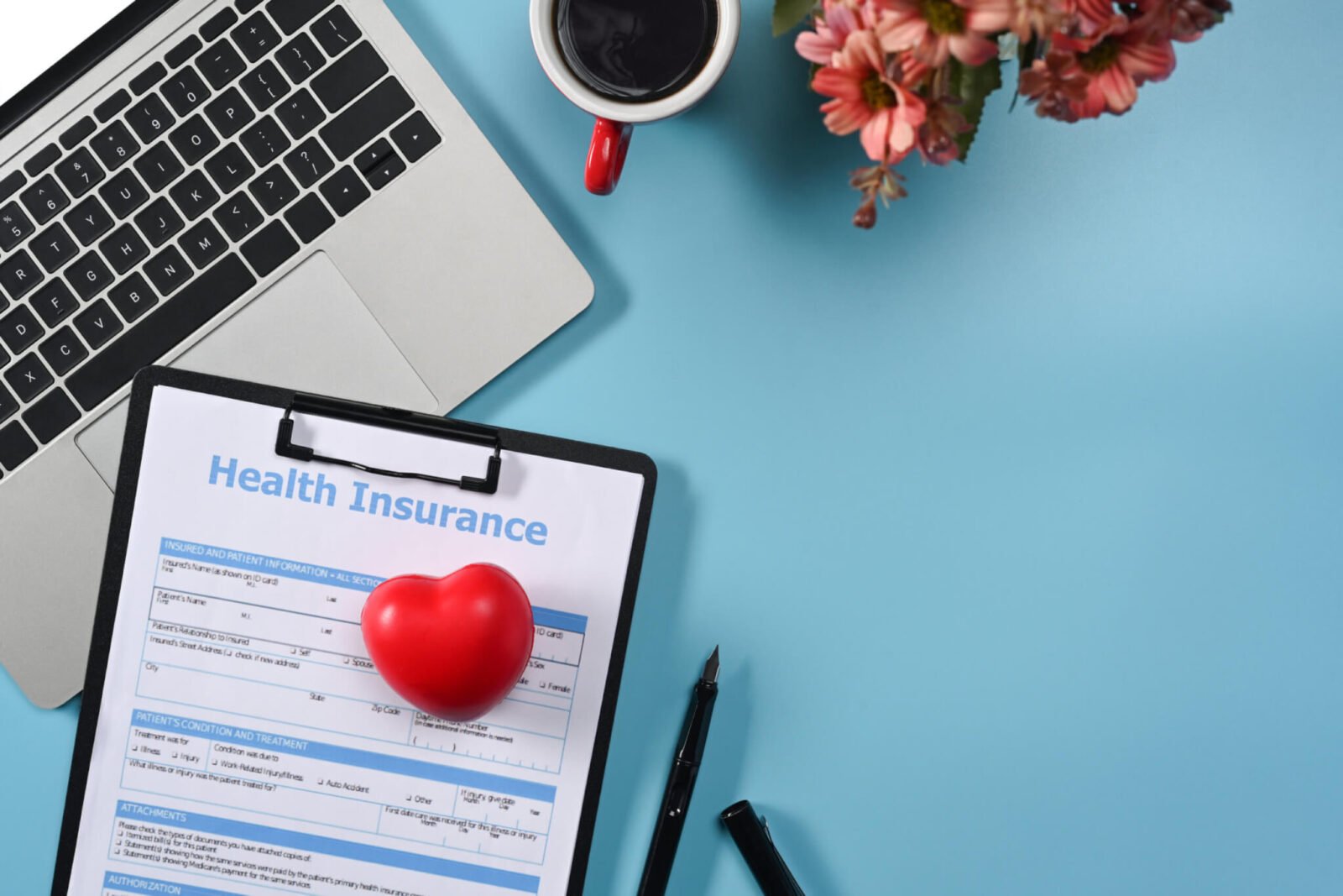 Health insurance claim form, computer, coffee, and flowers.