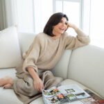 Tamsen Fadal relaxes on the couch wearing cream with a magazine