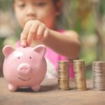 A young girl dressed in pink puts quarters into a pink piggy bank.