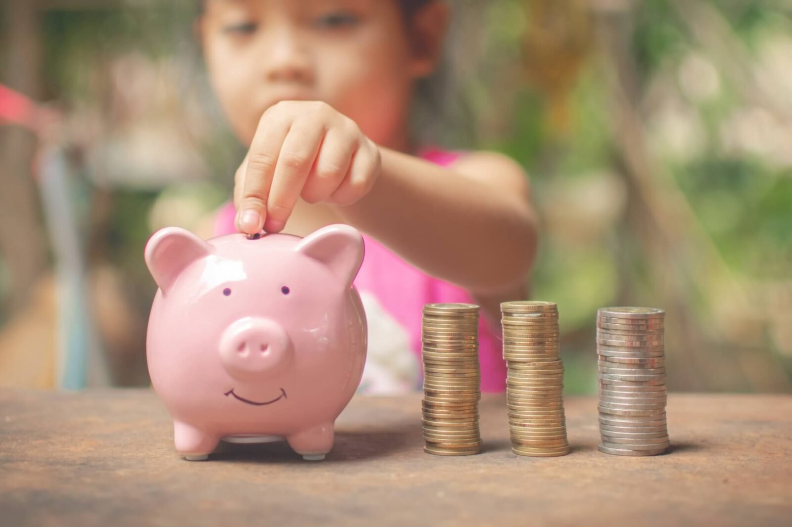 A young girl dressed in pink puts quarters into a pink piggy bank.