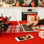 This is a close up of a person sitting at a laptop. You can only see their hands at the keyboard. The table is decorated for the holidays.