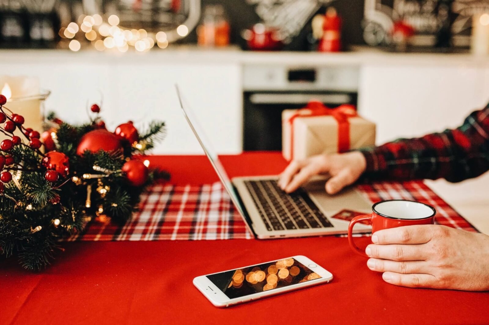 This is a close up of a person sitting at a laptop. You can only see their hands at the keyboard. The table is decorated for the holidays.