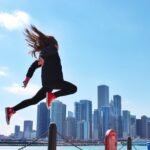 This is an image of a woman jumping in the air. The backdrop is a city.