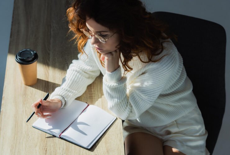 women writing in notebook with coffee