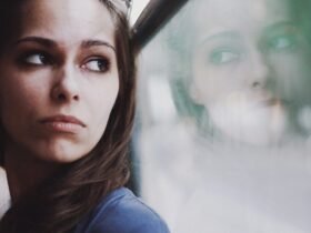 A woman with brown hair and a blue-grey top gazes out a hazy window and is contemplative about life.