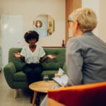 Women in therapy with arms raised talking to a psychologist.