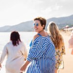 Women walking on the beach wearing sunglasses and smiling.