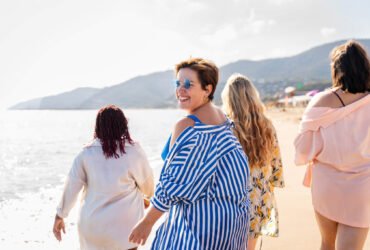 Women walking on the beach wearing sunglasses and smiling.