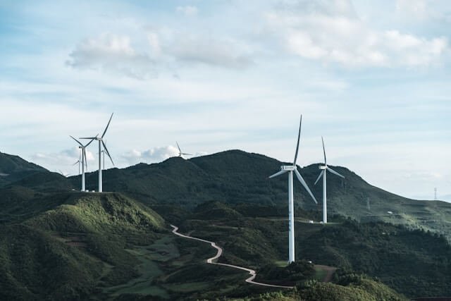Nine wind turbines set along a windy road through a green mountain pass.