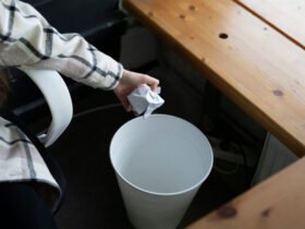 This is an image of a woman's hand throwing out a crumpled up piece of paper into a white trash can.