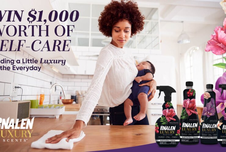 Image of a Black woman in a white shirt holding a baby cleaning a kitchen countertop with a white cloth. In the foreground are Pinalen Luxury Scents cleaning products. Text reads "Win $1,000 worth of self-care Adding a little luxury to the everyday Pinalen Luxury Scents"