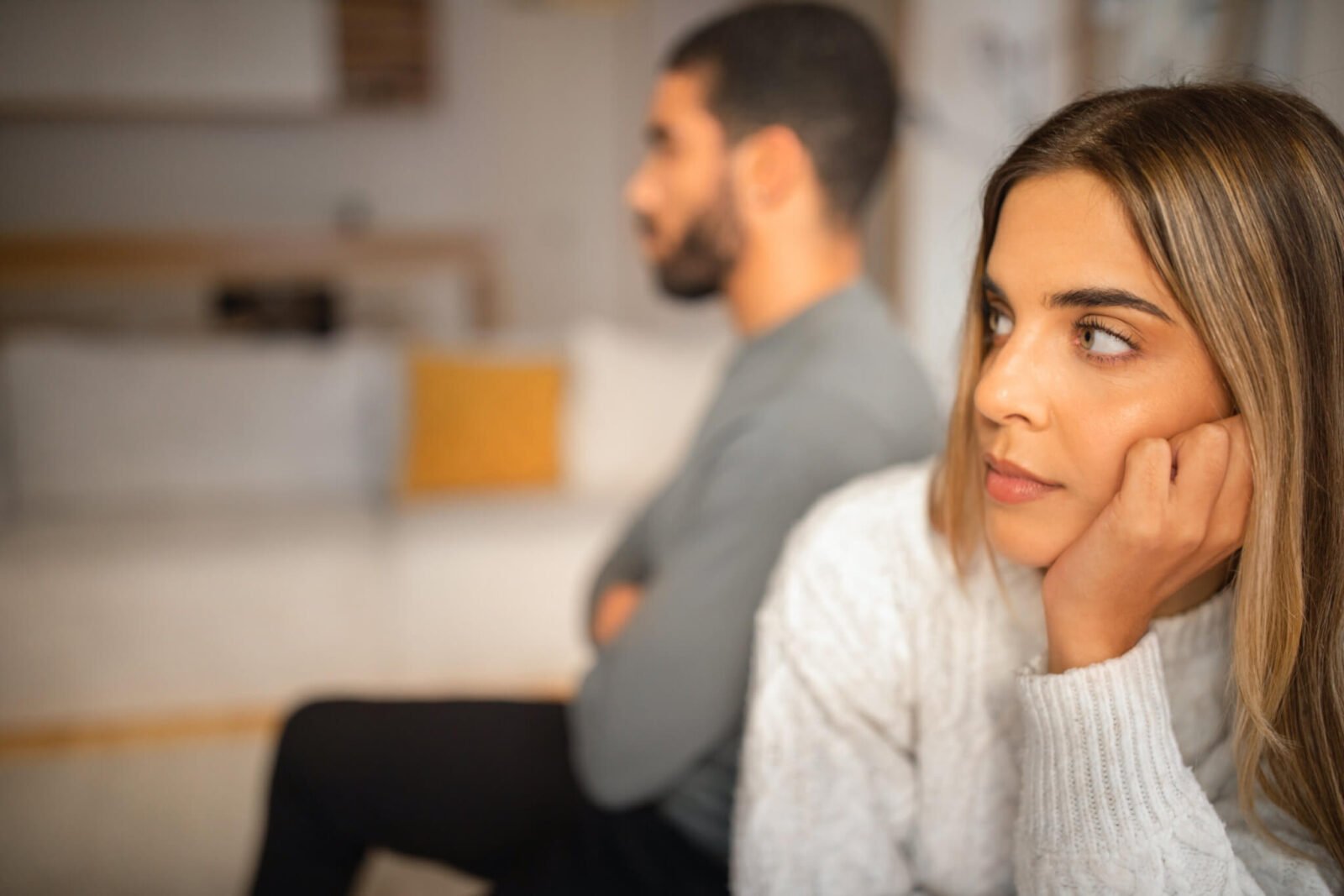 A woman is seen with her head in her hands, looking off in the distance. A man is behind her, with his arms crossed.