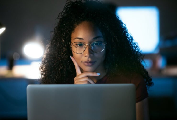 This is an image of a Black woman looking at a laptop computer. She has glasses on and appears to be thinking.