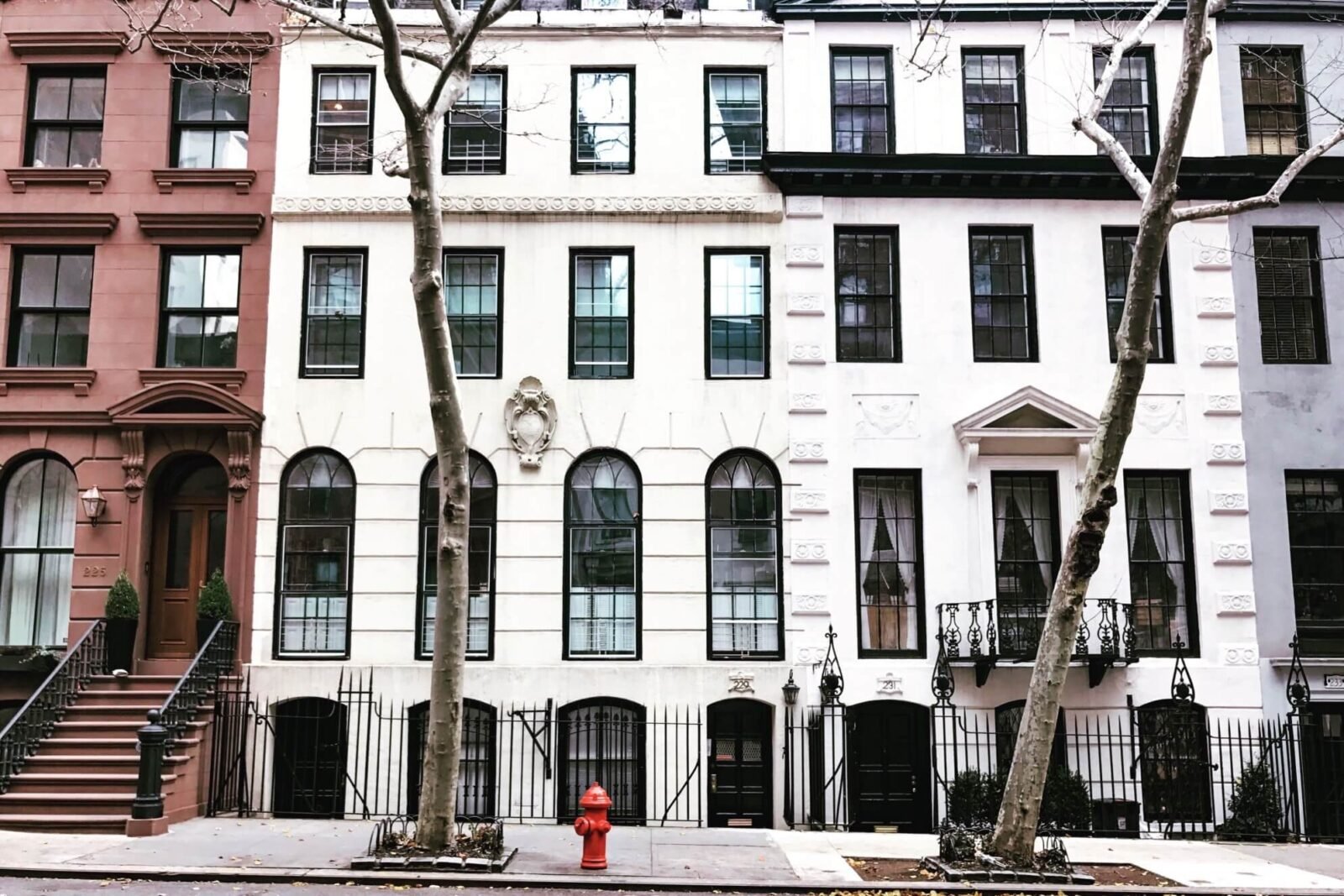 Image of houses on a street. The buildings are tall, with many windows. There are stairs leading up from the sidewalk to the entrances.
