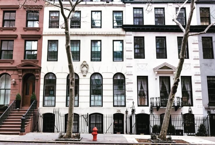 Image of houses on a street. The buildings are tall, with many windows. There are stairs leading up from the sidewalk to the entrances.