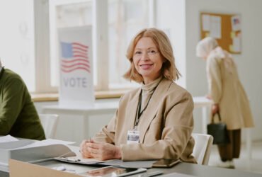 woman leading local government sitting at a table with a vote sign in the background