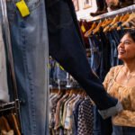 A young woman is in a secondhand store looking at jeans.