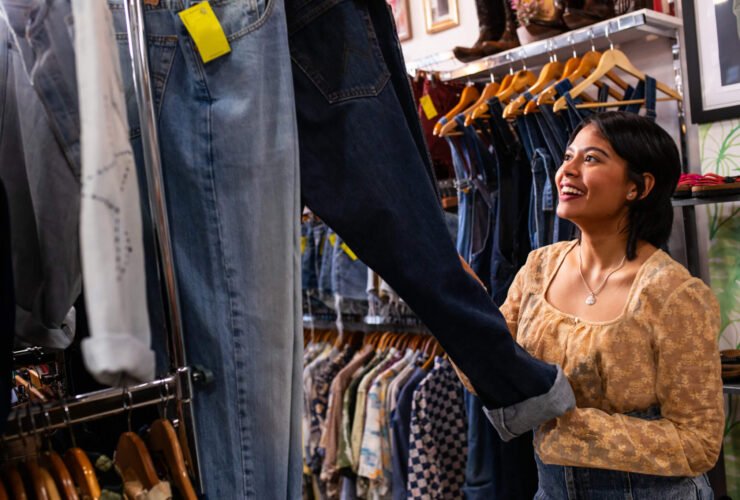 A young woman is in a secondhand store looking at jeans.