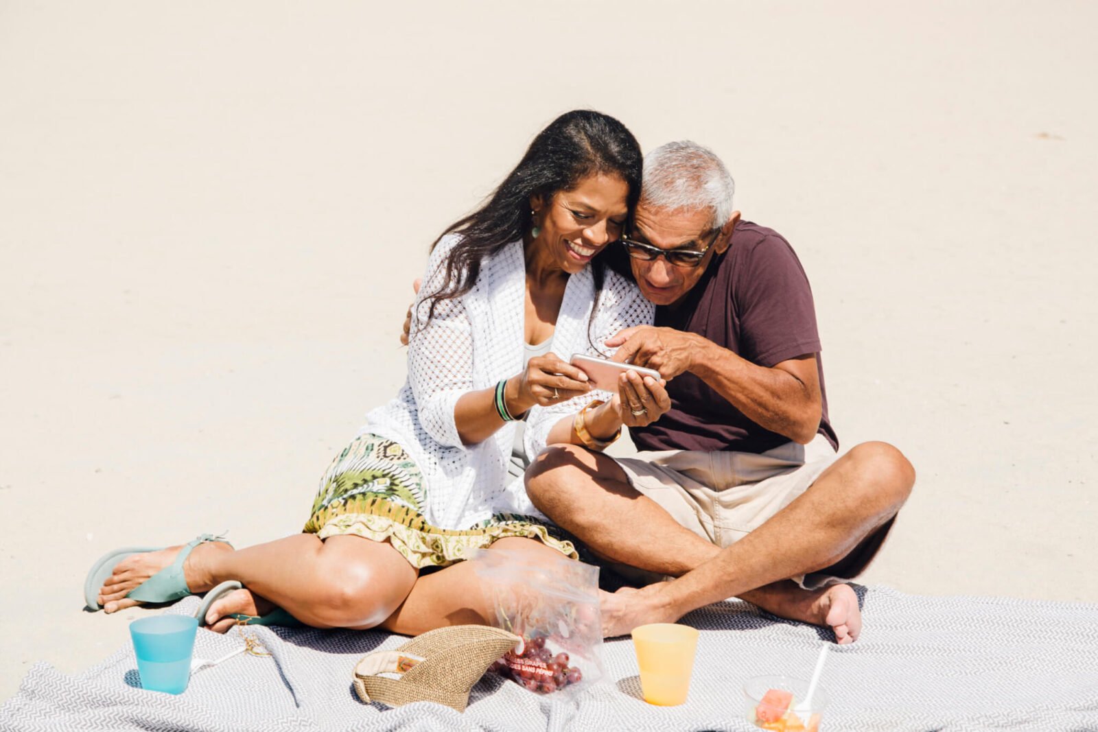 couple sitting on a beach with snacks smiling during their mini retirement