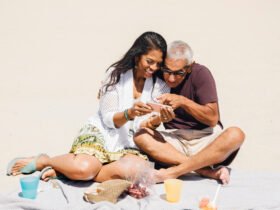couple sitting on a beach with snacks smiling during their mini retirement
